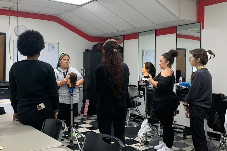 Cosmetology students gathered around an instructor's mannequin demo at Hyphen in Winter Park, FL, near Winter Garden
