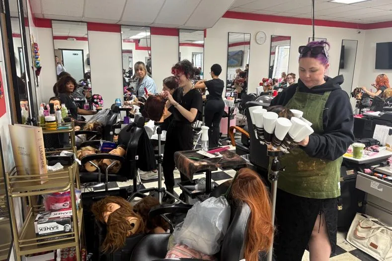 Cosmetology students working on mannequins in a busy classroom at Hyphen Beauty + Massage School in Winter Park, FL