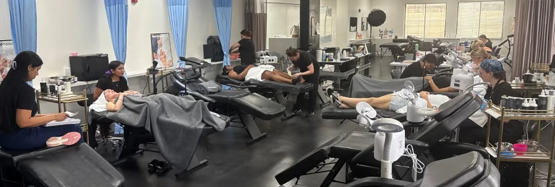 Esthetics classroom with rows of treatment beds and students at work at Hyphen Beauty + Massage School in Winter Park, FL