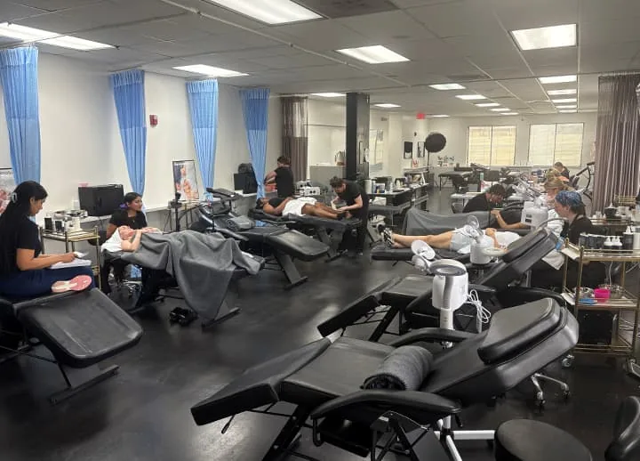 Esthetics classroom with rows of treatment beds and students at work at Hyphen Beauty + Massage School in Winter Park, FL