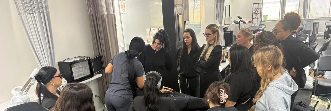 Esthetics students gathered around an instructor's treatment demo at Hyphen Beauty + Massage School in Winter Park, FL