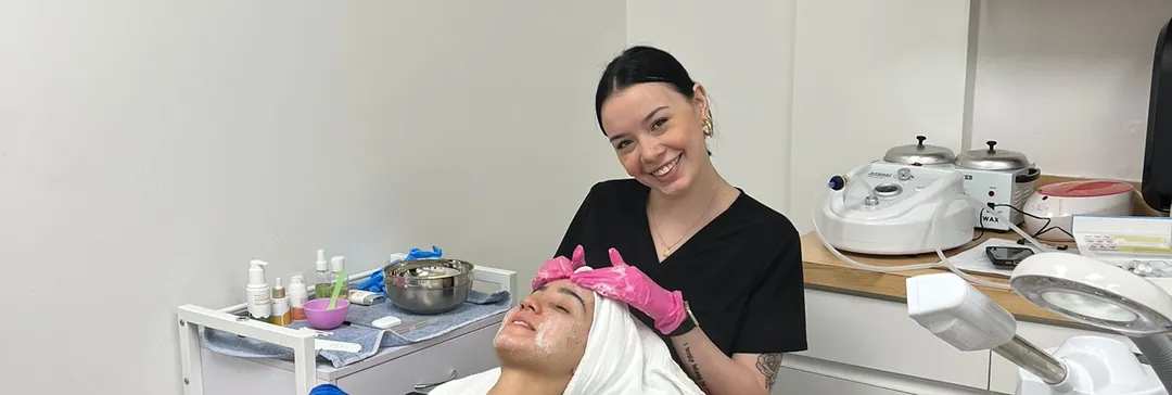 Esthetics student giving a client a facial on a treatment bed at Hyphen Beauty + Massage School