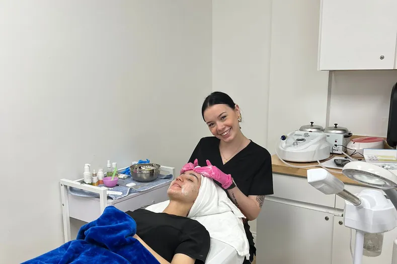 Esthetics student giving a client a facial on a treatment bed at Hyphen Beauty + Massage School