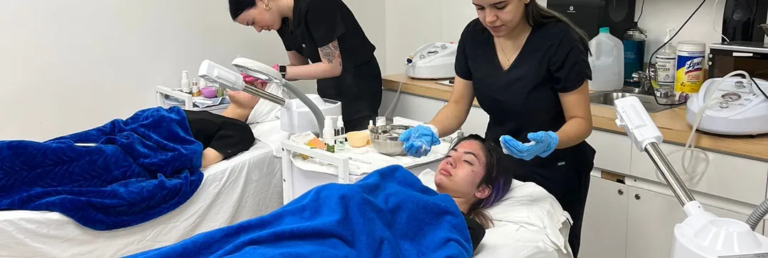 Esthetics students giving facials to clients in a treatment room at Hyphen Beauty + Massage School
