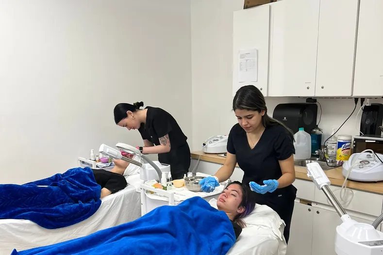 Esthetics students giving facials to clients in a treatment room at Hyphen Beauty + Massage School
