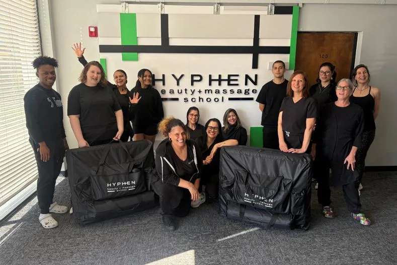 Massage class with their massage tables in front of the Hyphen sign at Hyphen Beauty + Massage School in Winter Park, FL