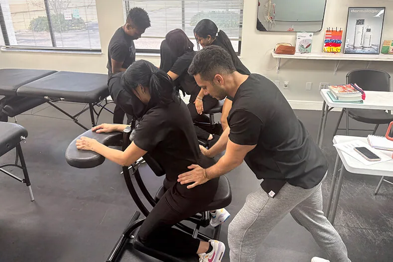 Massage student giving a classmate a chair massage at Hyphen Beauty + Massage School in Winter Park, FL