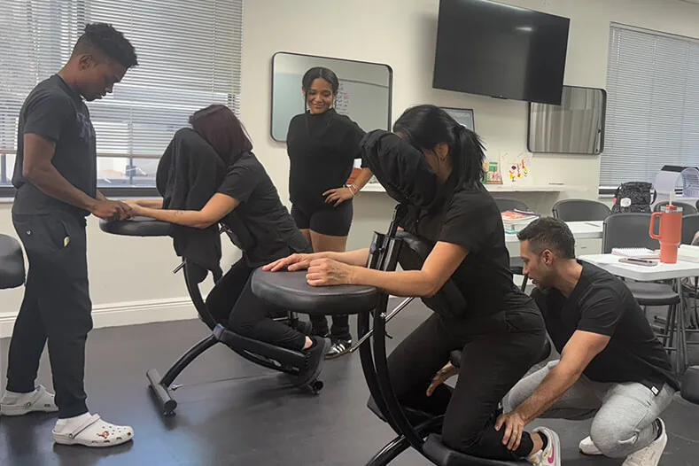 Massage students taking turns on massage chairs in class at Hyphen Beauty + Massage School in Winter Park, FL