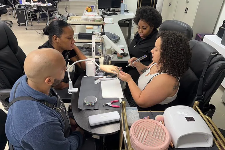 Nail tech students practicing on practice hands during class at Hyphen Beauty + Massage School in Winter Park, FL