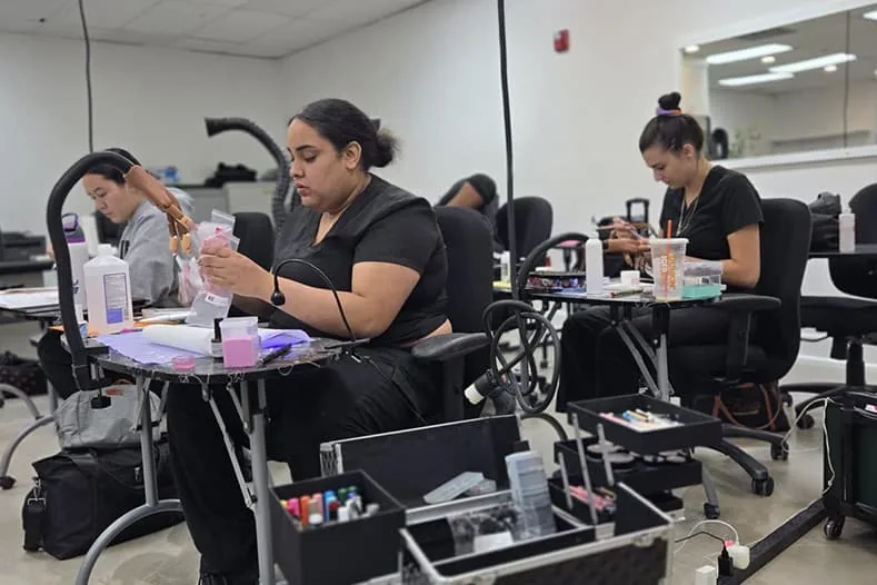 Nail tech students working on manicures at their stations at Hyphen Beauty + Massage School in Winter Park, FL, near Oviedo